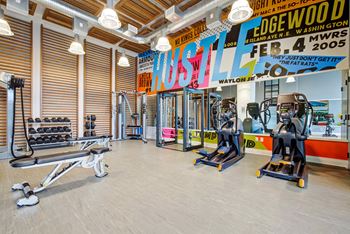 A gym with cardio machines and weights on the floor and a wall with a mural
